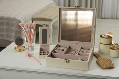 Photo of Elegant jewelry box with beautiful bijouterie and cosmetics on dressing table in bedroom