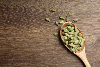 Photo of Spoon with dry cardamom pods on wooden table, top view. Space for text