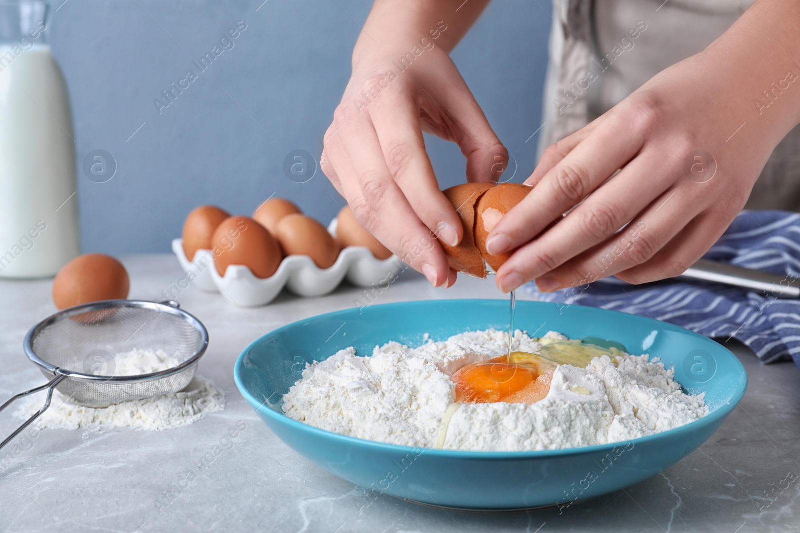 Photo of Woman preparing batter for thin pancakes at light grey table, closeup