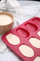 Photo of Baking mold for madeleine cookies with batter on white table, closeup