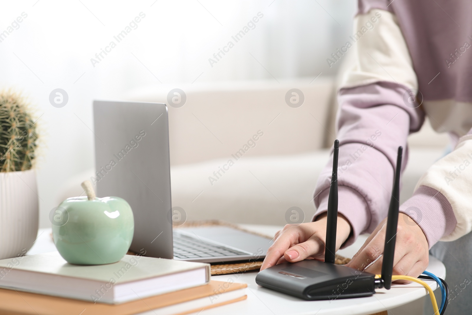 Photo of Woman connecting cable to Wi-Fi router at table indoors, closeup