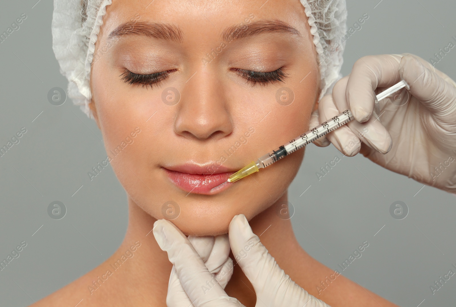 Photo of Young woman getting lips injection on grey background. Cosmetic surgery