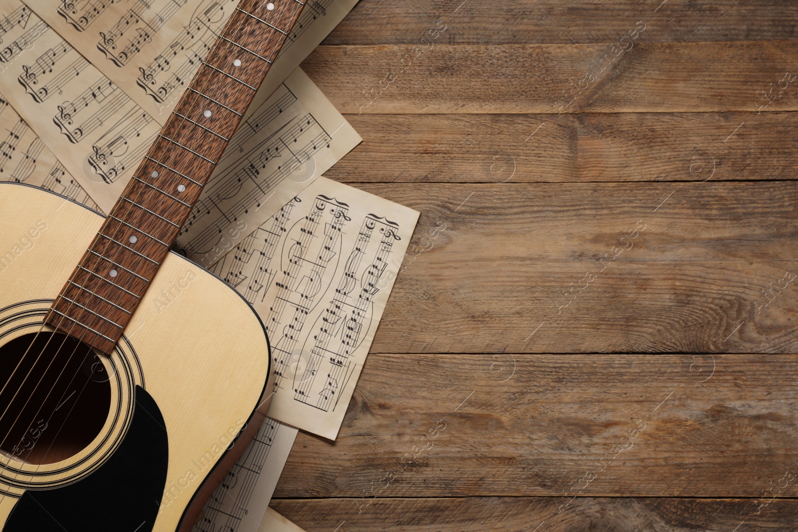 Photo of Paper sheets with music notes and acoustic guitar on wooden table, top view. Space for text