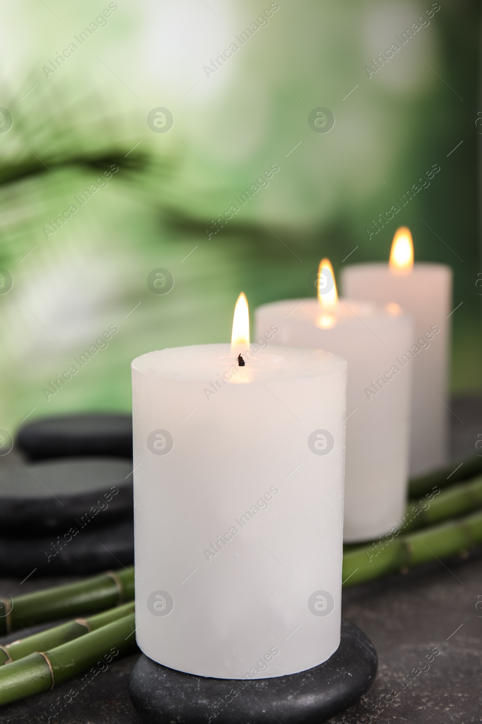 Photo of Burning candles, spa stones and bamboo sprouts on grey table against blurred green background