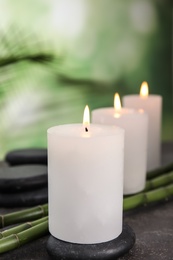 Photo of Burning candles, spa stones and bamboo sprouts on grey table against blurred green background