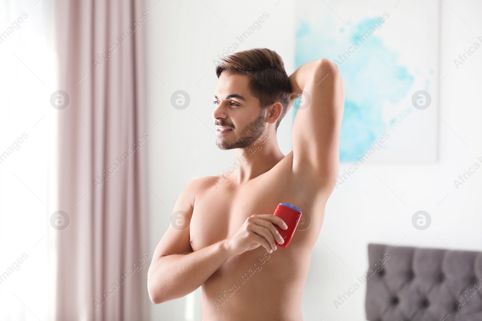 Photo of Handsome young man applying deodorant in room