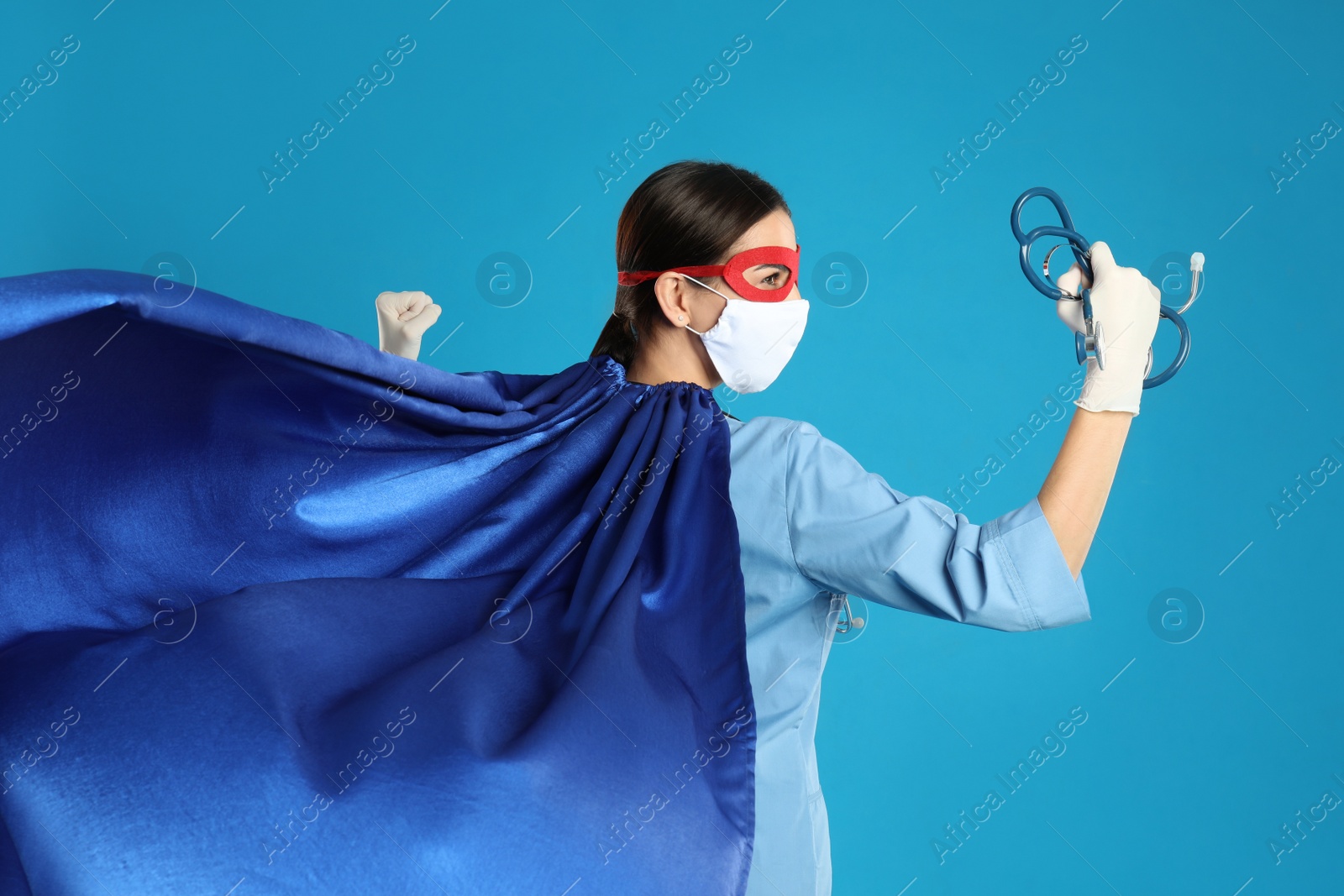 Photo of Doctor dressed as superhero posing on light blue background. Concept of medical workers fighting with COVID-19