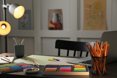 Photo of Artist's workplace with soft pastels, laptop and drawing pencils on table indoors