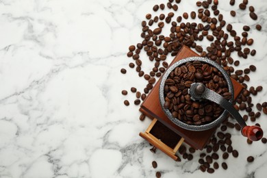 Vintage manual coffee grinder with beans on white marble table, flat lay. Space for text