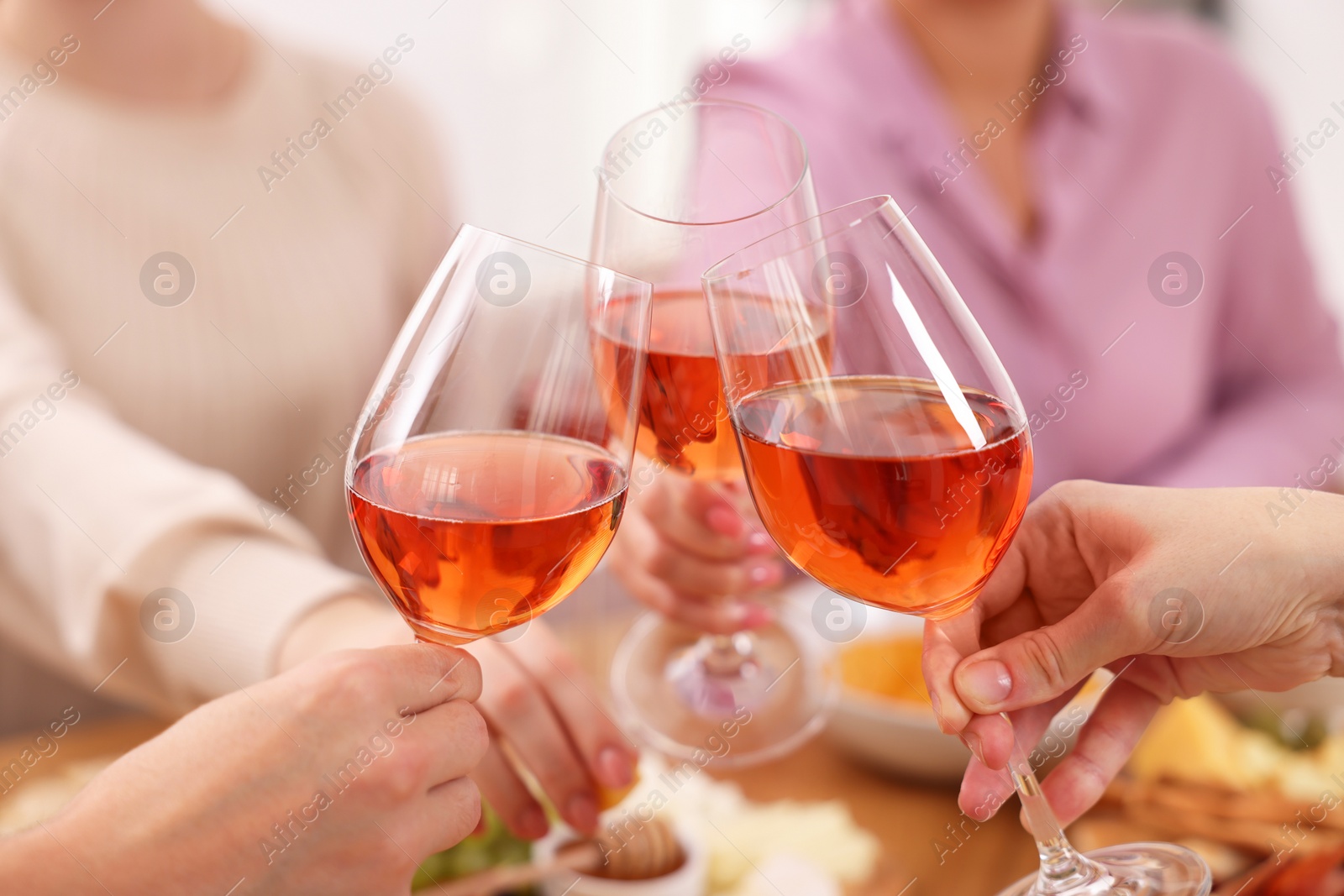 Photo of People clinking glasses with rose wine above table indoors, closeup