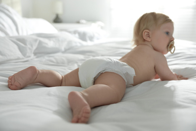 Photo of Cute little baby in diaper in bedroom, focus on legs