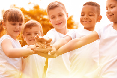 Image of Group of children joining hands in park on sunny day. Volunteering with kids