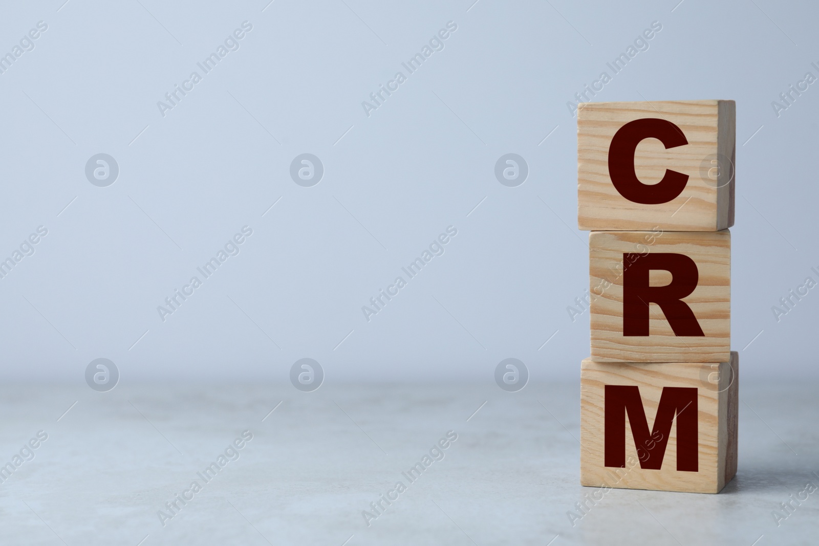 Photo of Abbreviation CRM of wooden cubes on grey table against light background, space for text. Customer Relationship Management