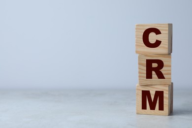 Photo of Abbreviation CRM of wooden cubes on grey table against light background, space for text. Customer Relationship Management