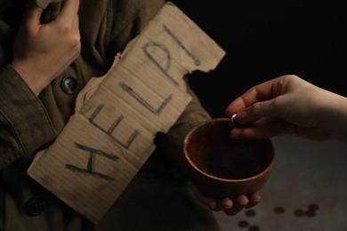 Woman giving coins to homeless with help sign, closeup. Charity and donation