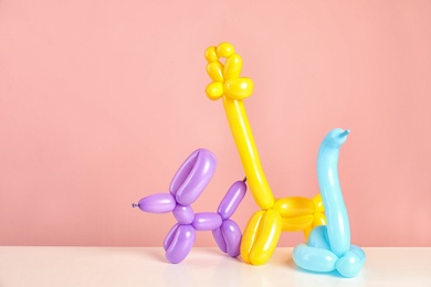 Photo of Animal figures made of modelling balloons on table against color background. Space for text