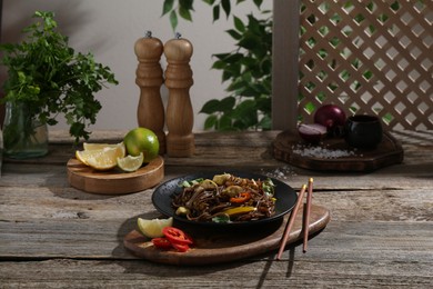 Photo of Stir-fry. Tasty noodles with meat and vegetables served on wooden table