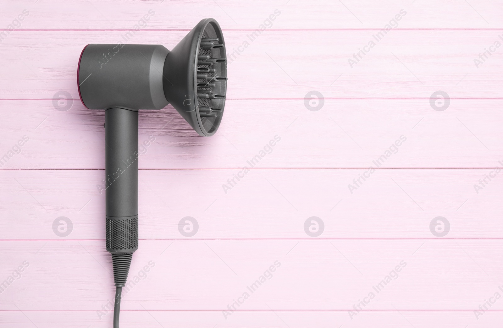 Photo of Hair dryer on pink wooden table, top view with space for text. Professional hairdresser tool