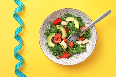 Bowl with fresh vegetable salad and measuring tape on color background, top view. Healthy diet