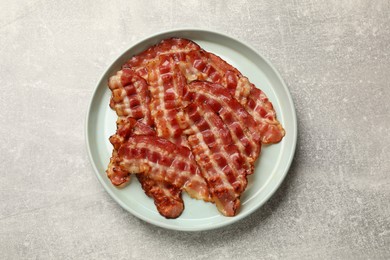 Photo of Plate with fried bacon slices on grey textured table, top view