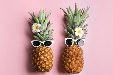 Funny pineapples with sunglasses and plumeria flowers on pink background, flat lay. Creative concept