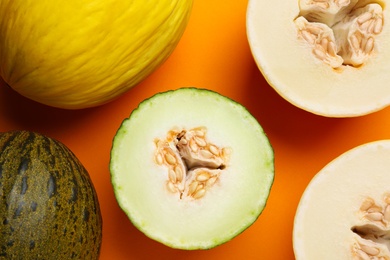 Photo of Ripe tasty melons on orange background, flat lay