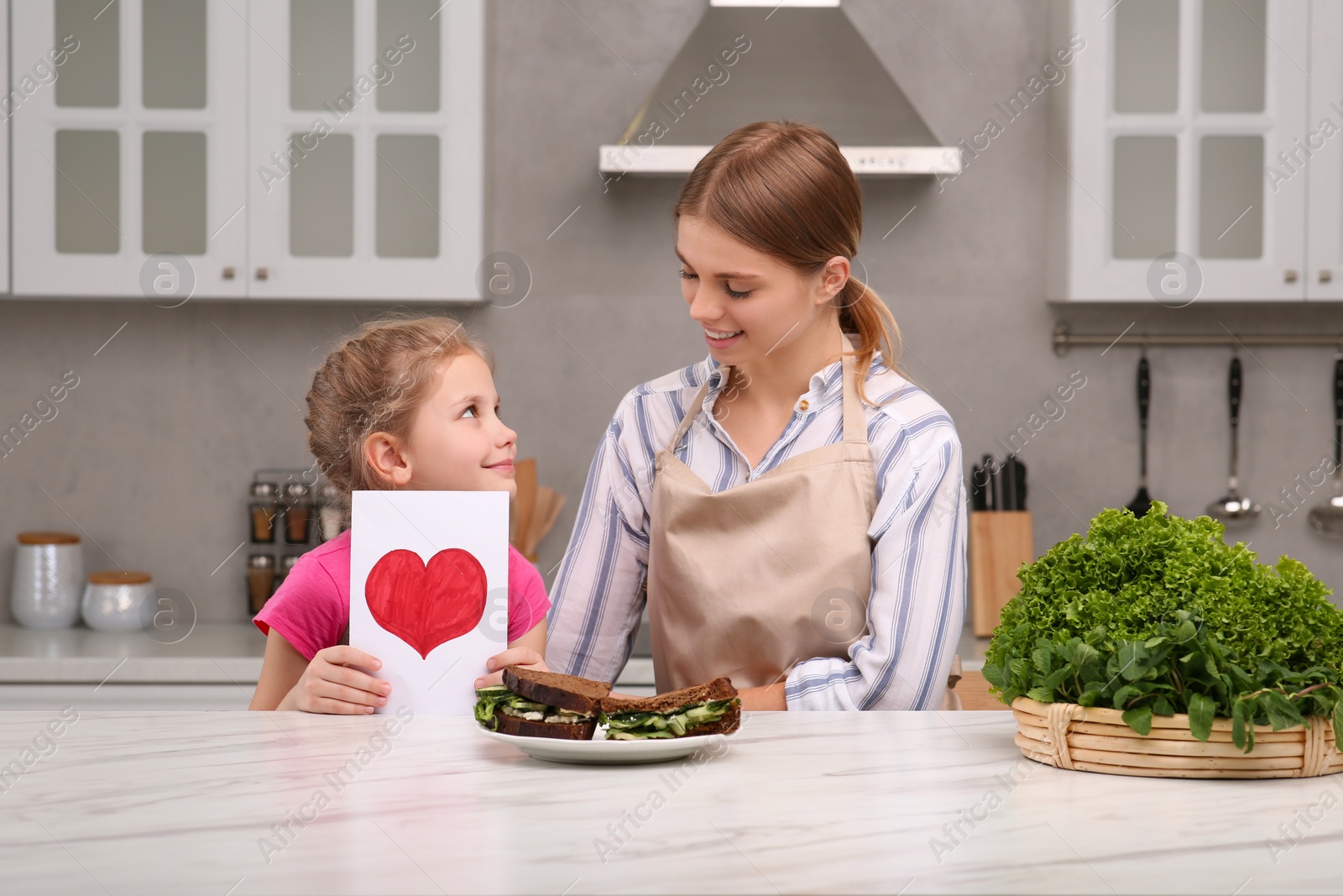 Photo of Little daughter congratulating mom with greeting card in kitchen. Happy Mother's Day