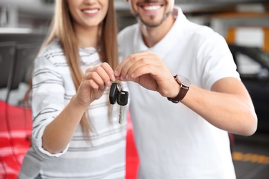 Woman and man with car keys in modern auto dealership, closeup