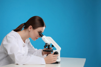 Photo of Scientist using modern microscope at table against blue background, space for text. Medical research