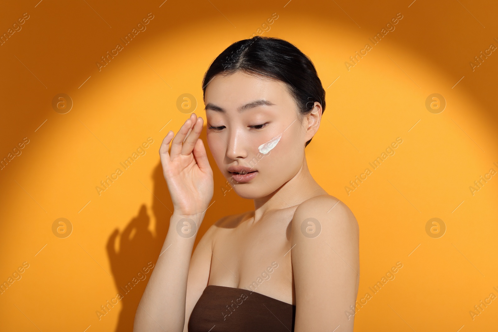 Photo of Beautiful young woman in sunlight with sun protection cream on her face against orange background