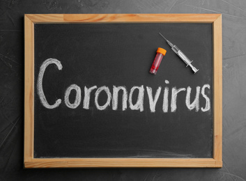 Chalkboard with word CORONAVIRUS, test tube and syringe on grey table, top view