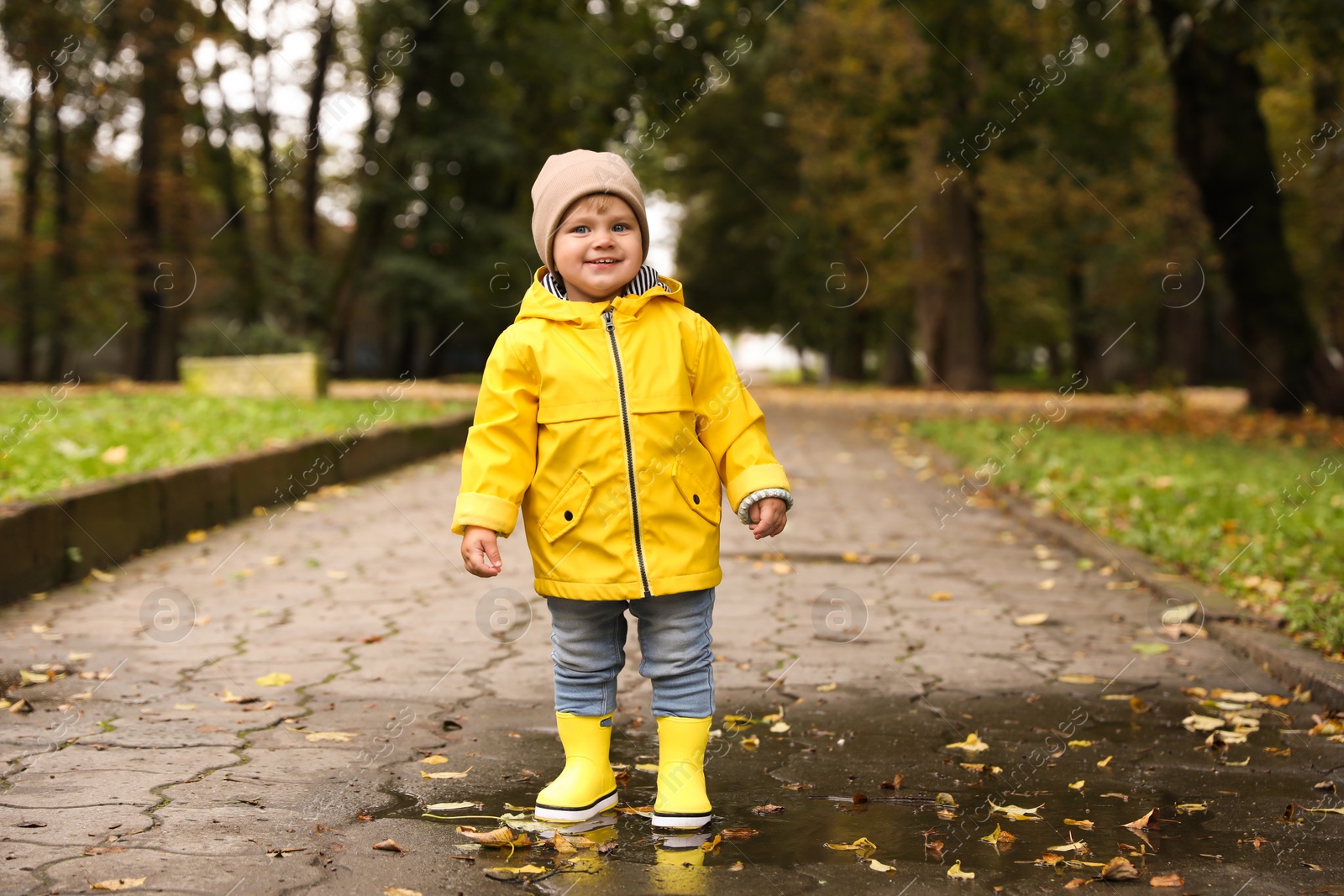 Photo of Cute little girl standing in puddle outdoors