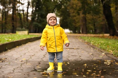 Photo of Cute little girl standing in puddle outdoors