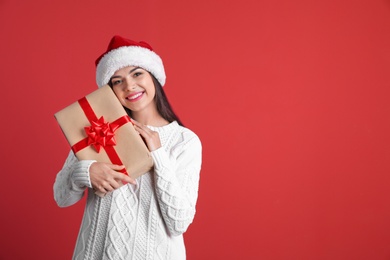 Photo of Young beautiful woman in Santa hat with gift box on color background. Christmas celebration