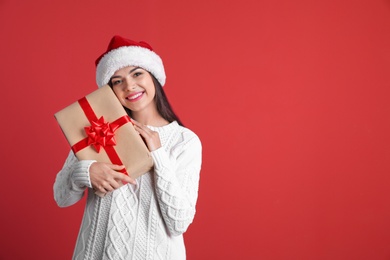 Young beautiful woman in Santa hat with gift box on color background. Christmas celebration