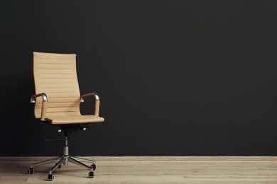 Photo of Comfortable office chair near black wall indoors. Space for text