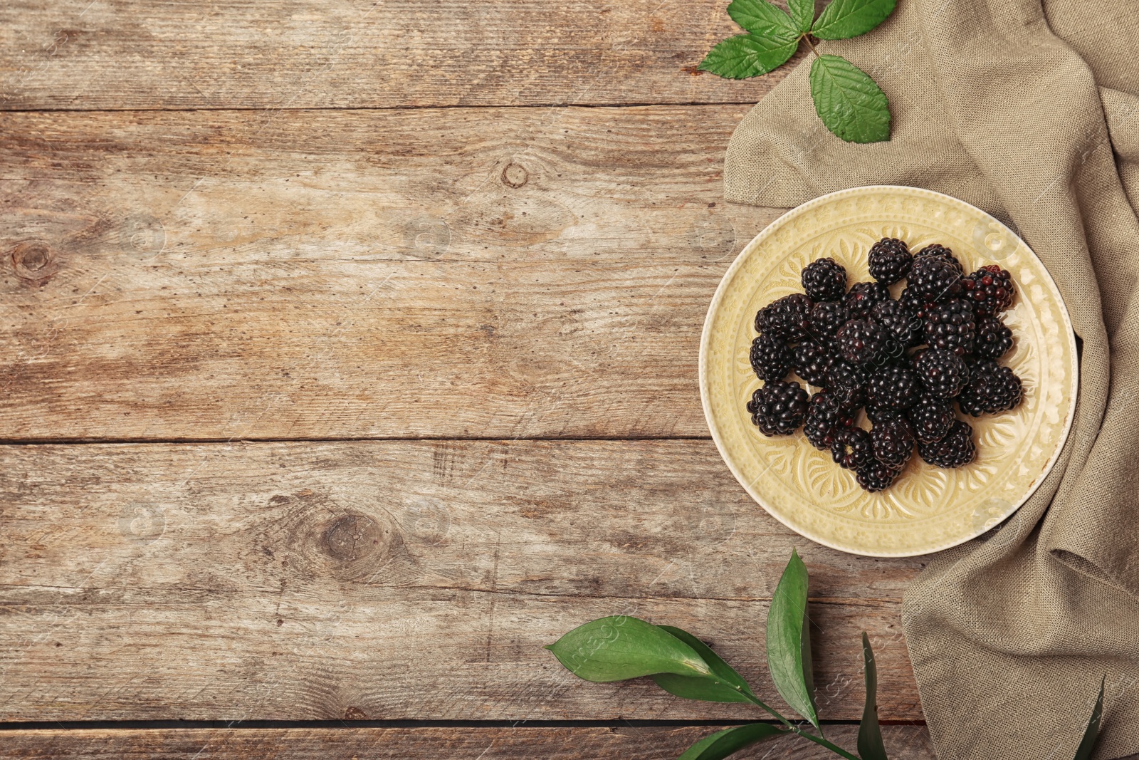 Photo of Flat lay composition with plate of fresh blackberry and space for text on wooden background