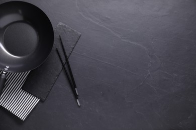 Empty iron wok and chopsticks on black table, top view. Space for text