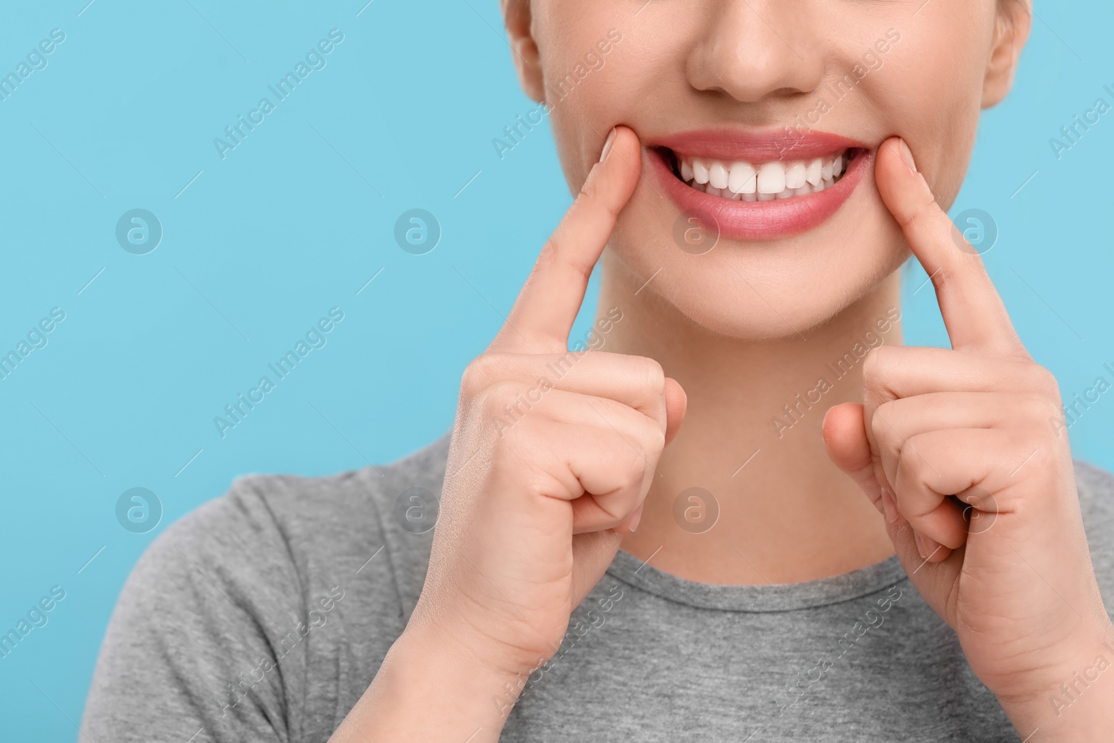 Photo of Woman showing her clean teeth on light blue background, closeup. Space for text