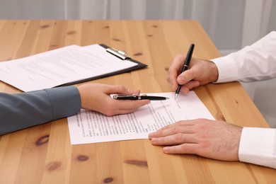 Photo of Businesspeople signing contract at wooden table in office, closeup of hands