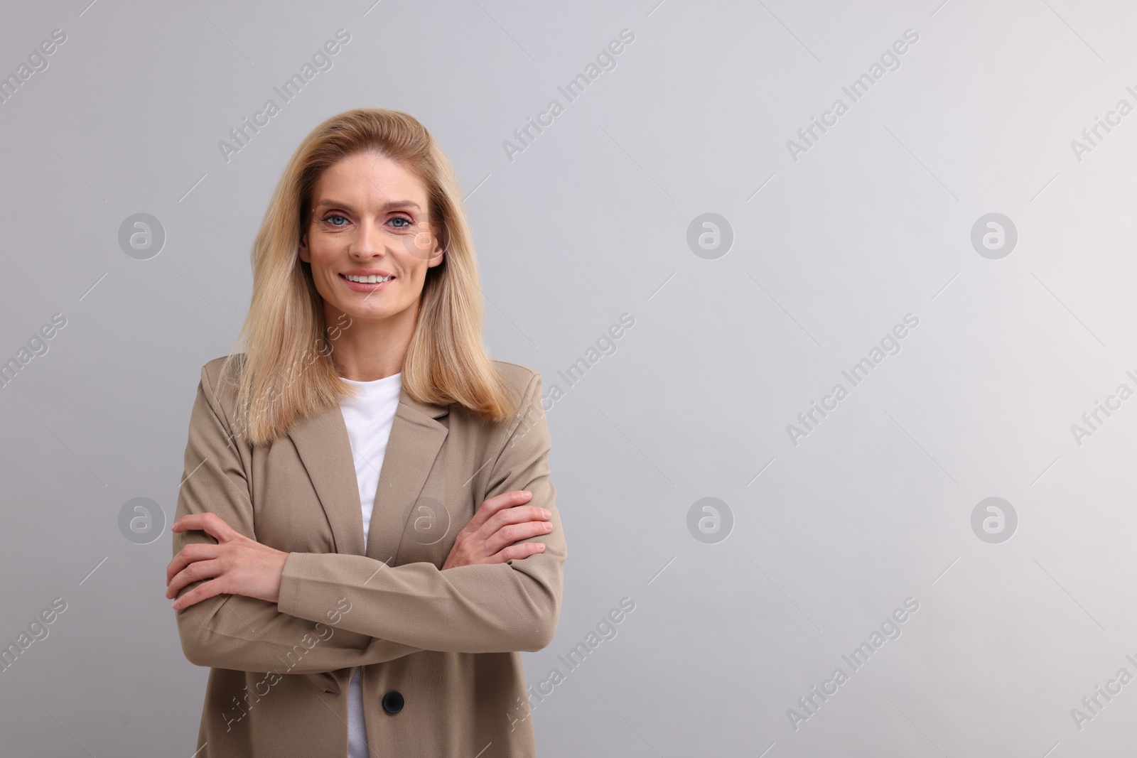 Photo of Portrait of smiling middle aged businesswoman with crossed arms on light grey background. Space for text