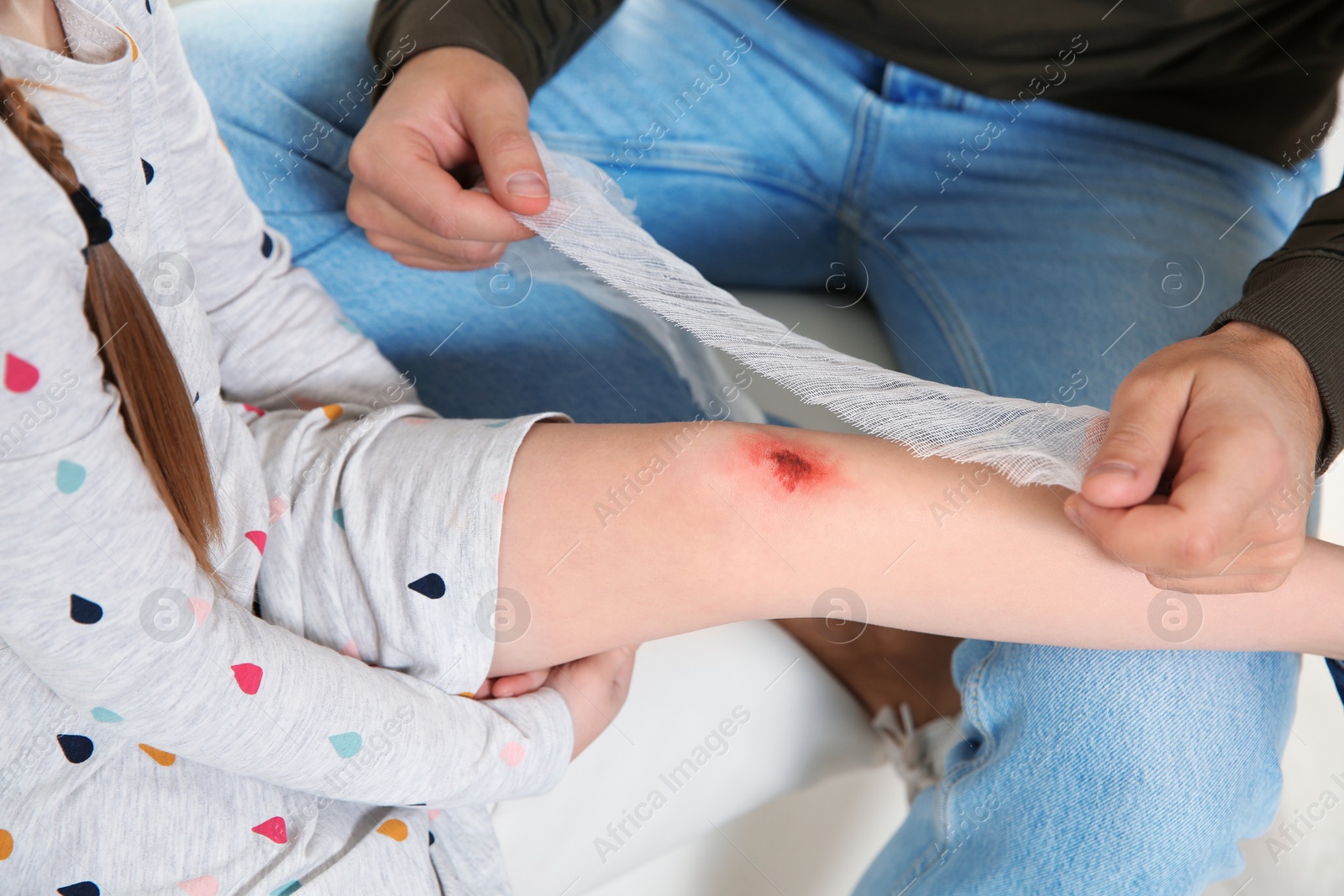 Photo of Father applying bandage on daughter's injured knee at home, closeup. First aid