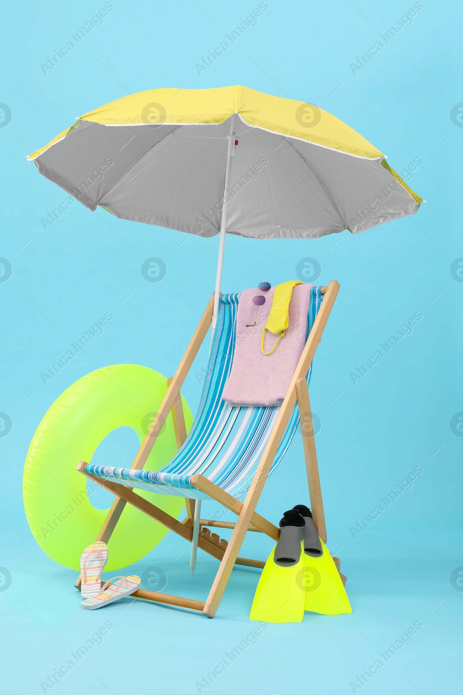 Deck chair, umbrella and beach accessories against light blue background. Summer vacation Photo of Deck chair, umbrella and beach accessories against light blue background. Summer vacation