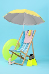 Photo of Deck chair, umbrella and beach accessories against light blue background. Summer vacation
