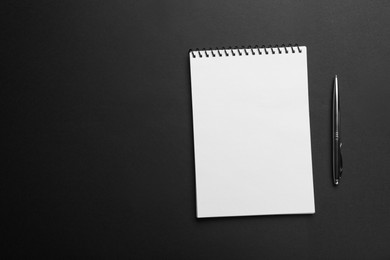 Photo of Notebook and pen on black background, top view. Space for text