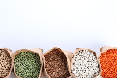 Photo of Different types of legumes  and cereals in paper bags on white background, top view. Organic grains