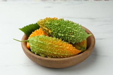 Photo of Wooden bowl with fresh bitter melons on white marble table, closeup