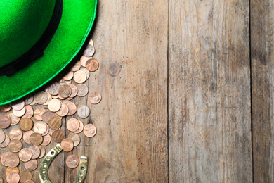 Gold coins, horseshoe and green leprechaun hat on wooden table, flat lay with space for text. St. Patrick's Day celebration