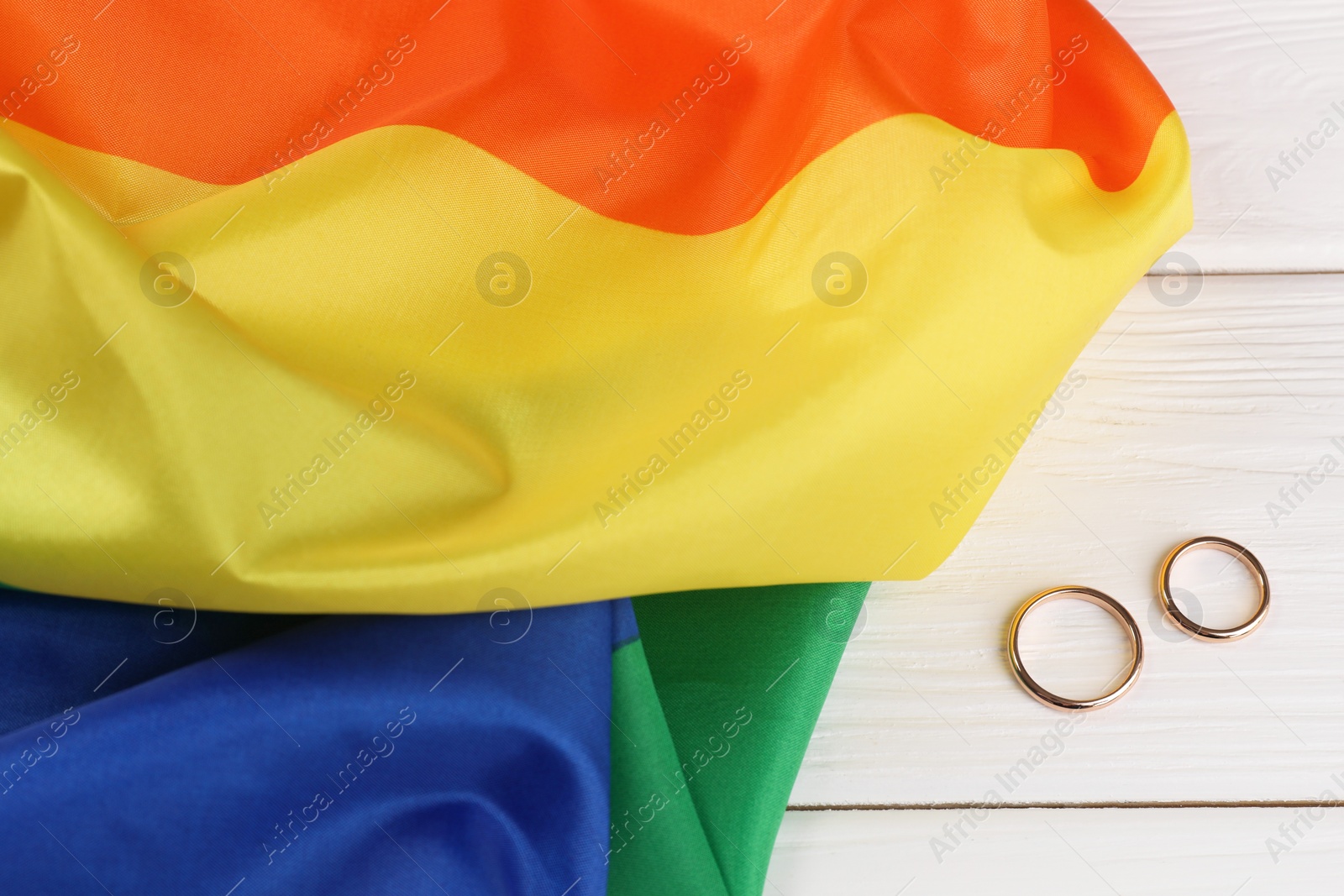 Photo of Rainbow LGBT flag and wedding rings on white wooden table, top view