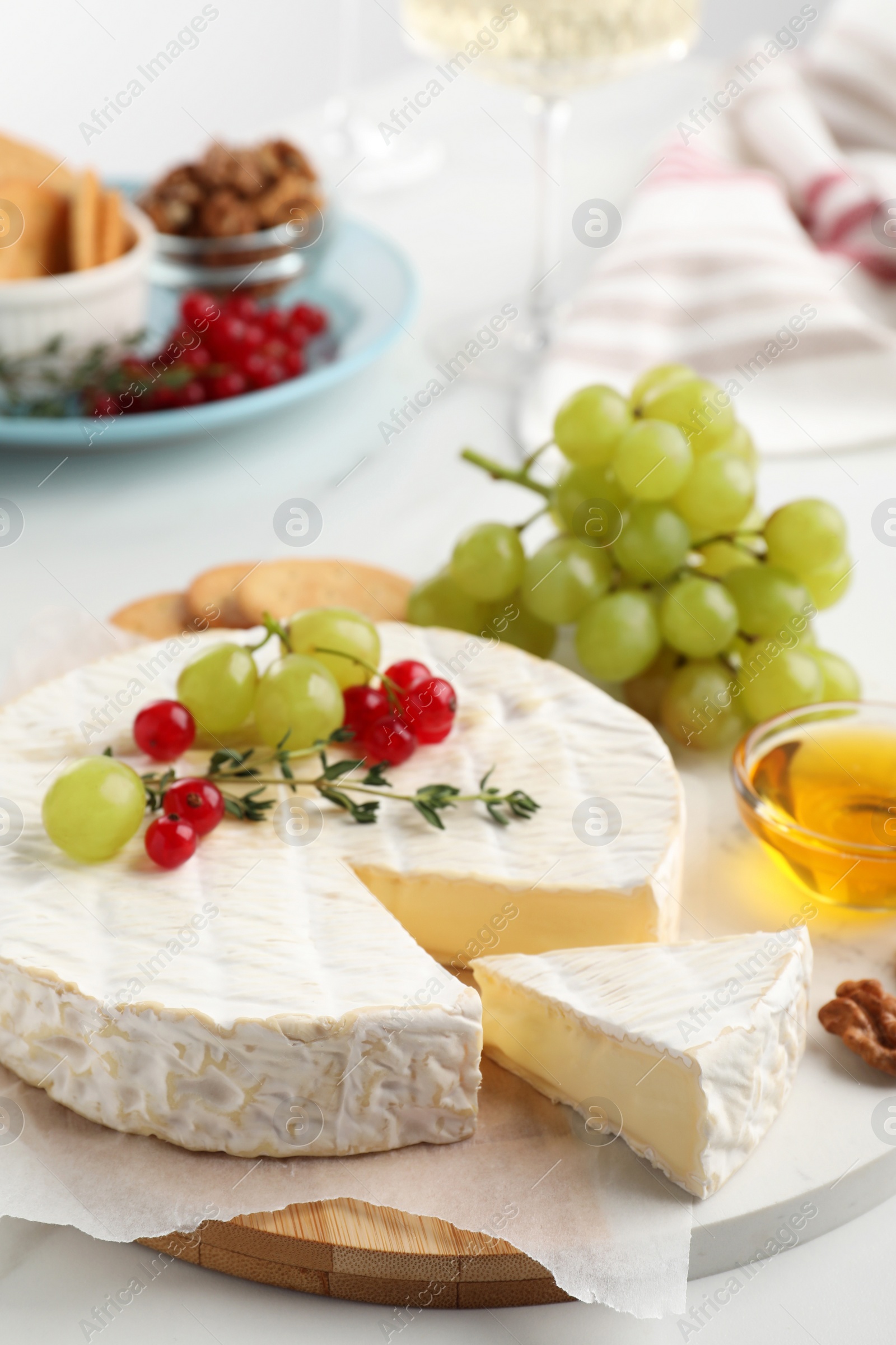 Photo of Brie cheese served with honey and berries on white table, closeup